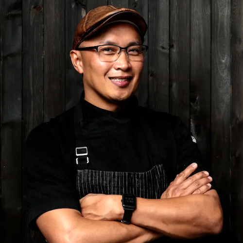 Person wearing a black apron and brown cap with a dark background
